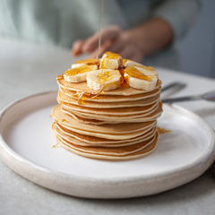 A stack of pancakes with banana toppings and syrup served in a plate