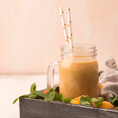 A jar of orange coloured drink with two straws in it served on a tray that has Oranges with leaves