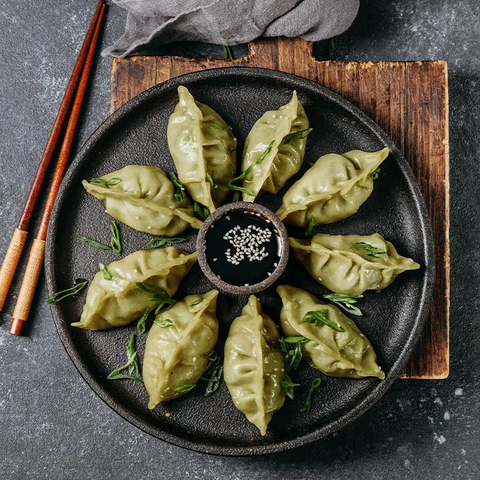 nine Steamed dim sums served in a plate with soya sauce in centre and two chopsticks on the side 