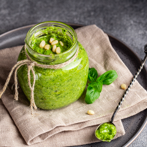 Green pesto in a glass jar with nut topping